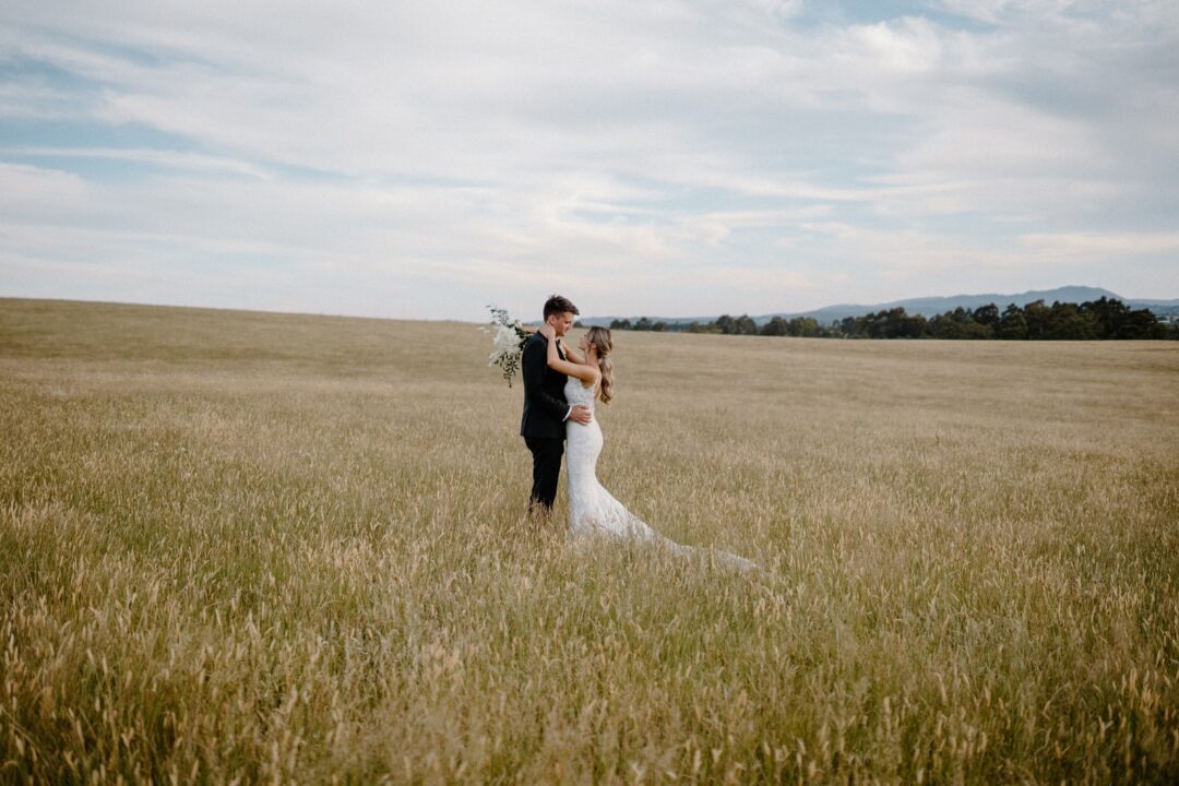 woman in white wedding gown holding man in black suit on green grass field during daytime